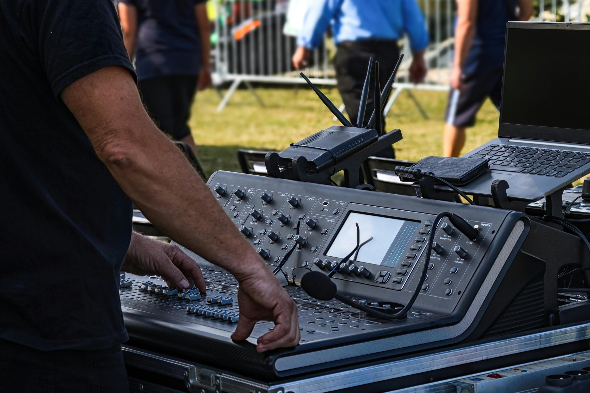 Un ingénieur du son manipule une console de mixage pour l'installation d'un concert en plein air. Technologie et musique s'unissent.