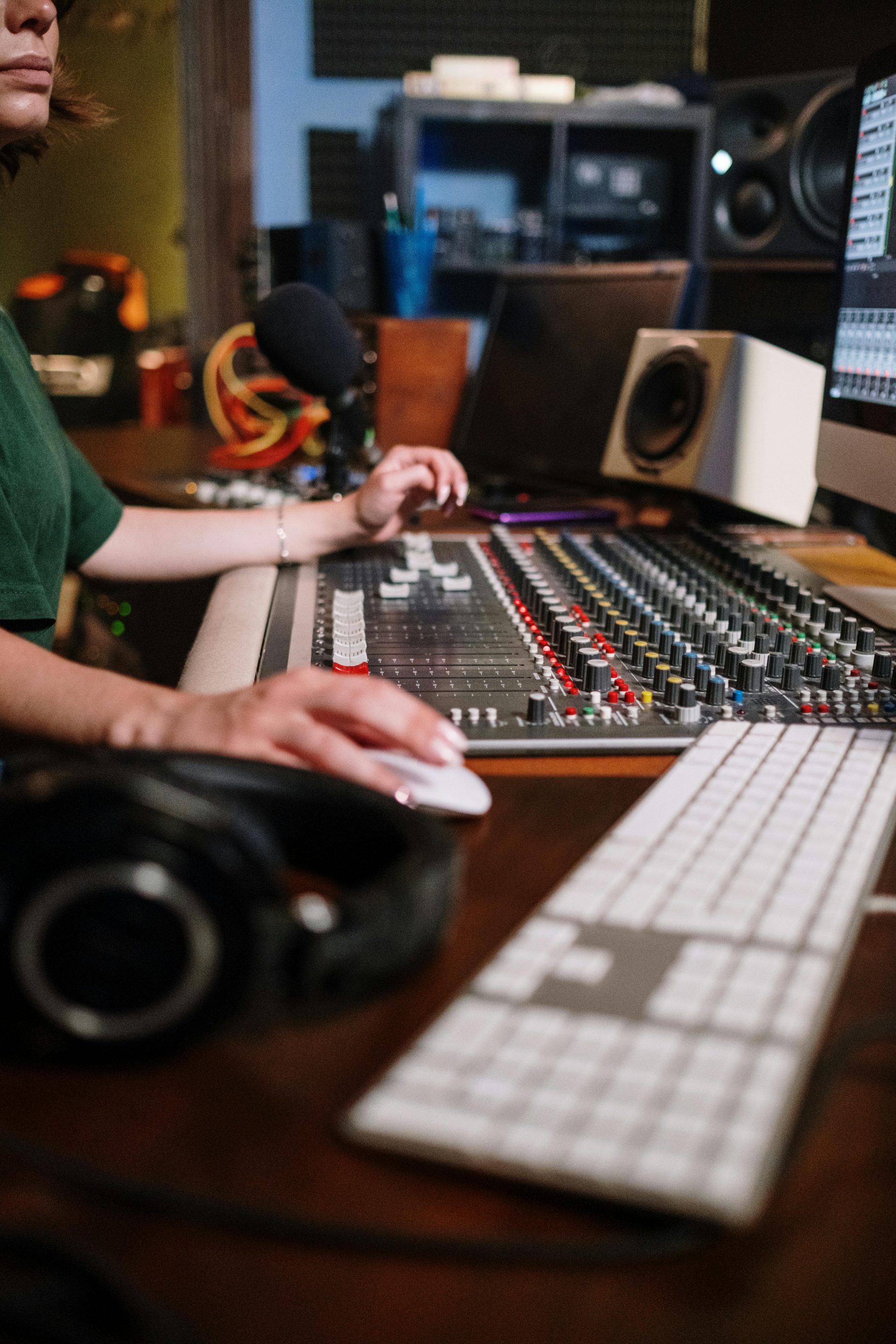 Une femme travaille sur une console de mixage audio dans un studio de son professionnel, réglant les commandes et utilisant une souris d'ordinateur.
